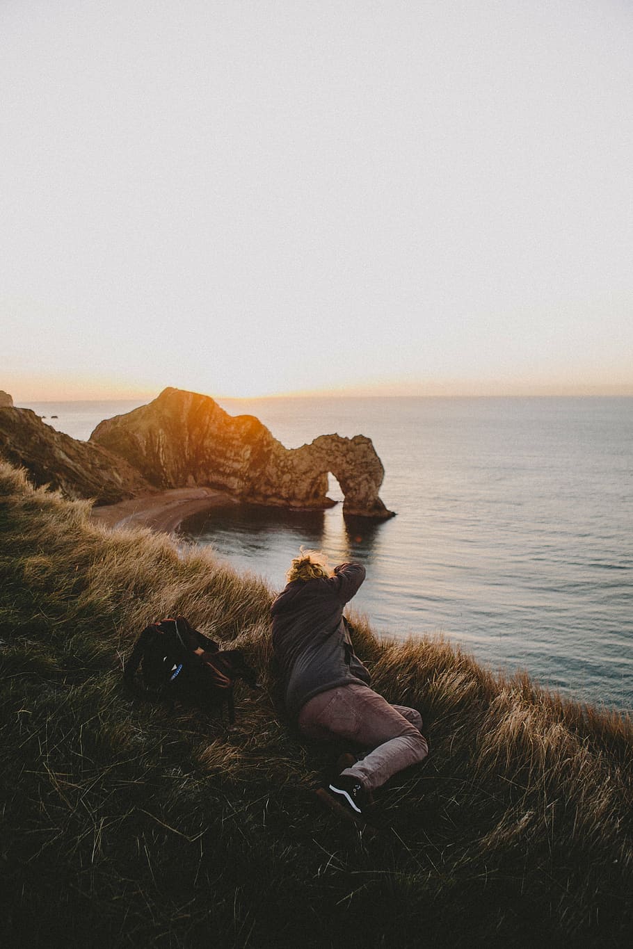 person laying in front of body of water, grass, blur, coast, sea