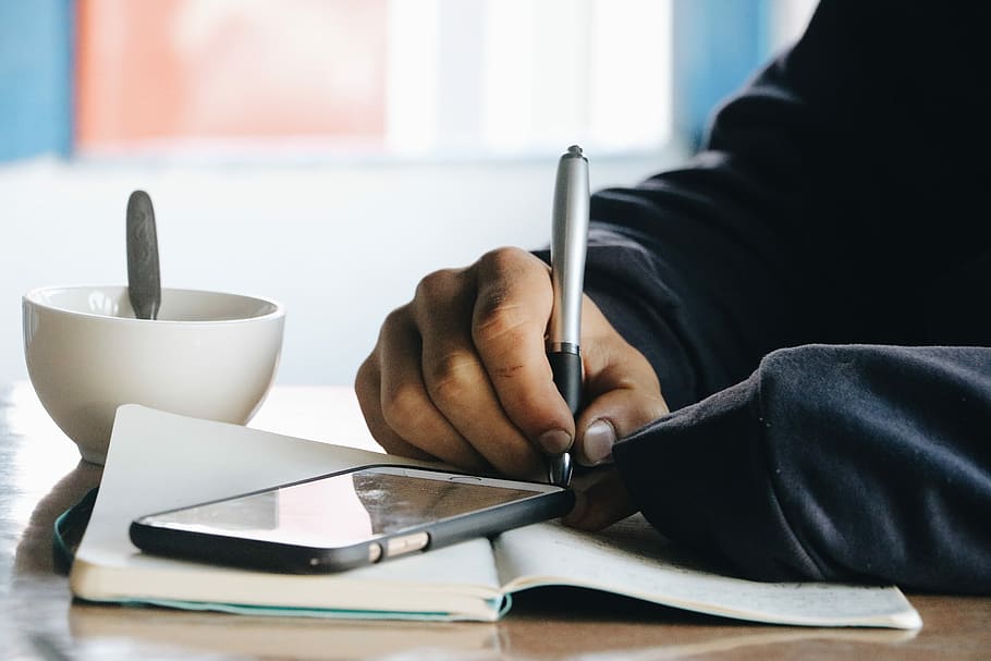 person holding pen, person writing on notebook, hand, cup, spoon HD wallpaper