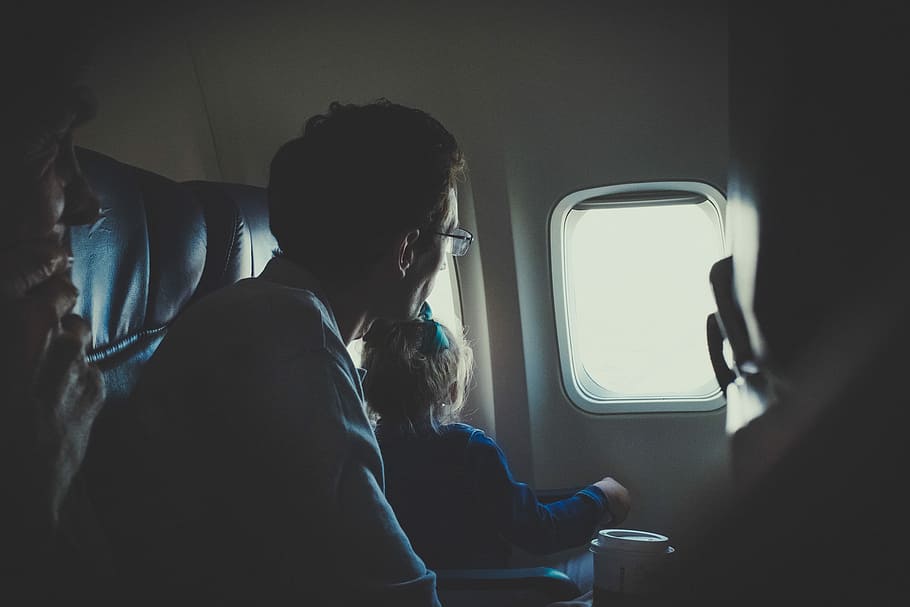 man and girl sitting inside airplane during daytime, girl and man looking to passenger plane window close-up photo