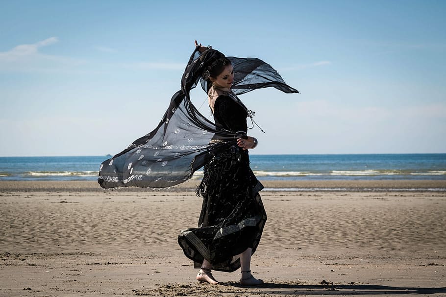 woman in black long dress holding scarf standing on seashore HD wallpaper