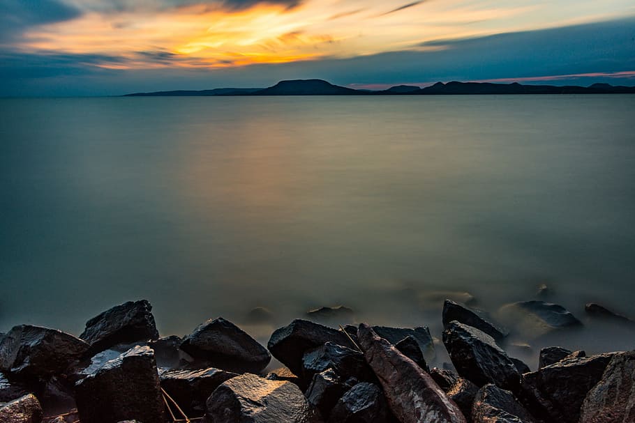 body of water under orange sunset, gray rock formation during daytime HD wallpaper