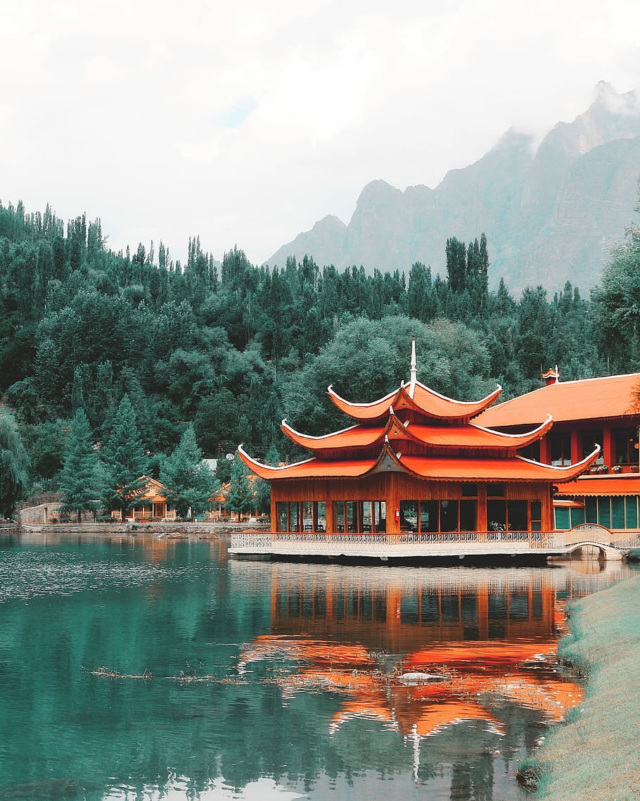 orange wooden building near green trees at daytime, red pagoda near body of water under white clouds HD wallpaper