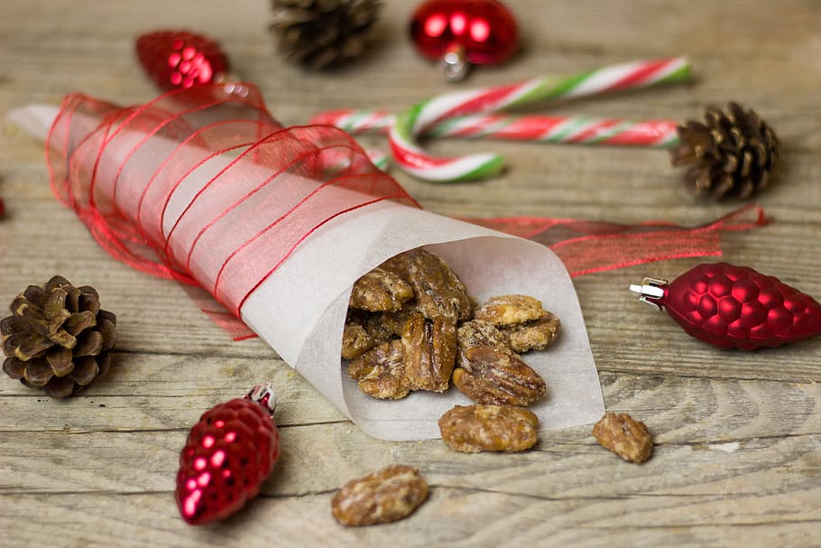brown nuts on paper cone placed on brown wooden surface surrounded by pinecones HD wallpaper