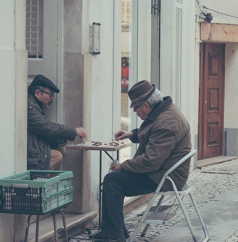 man sitting on step stool playing Chinese checkers with another man HD wallpaper