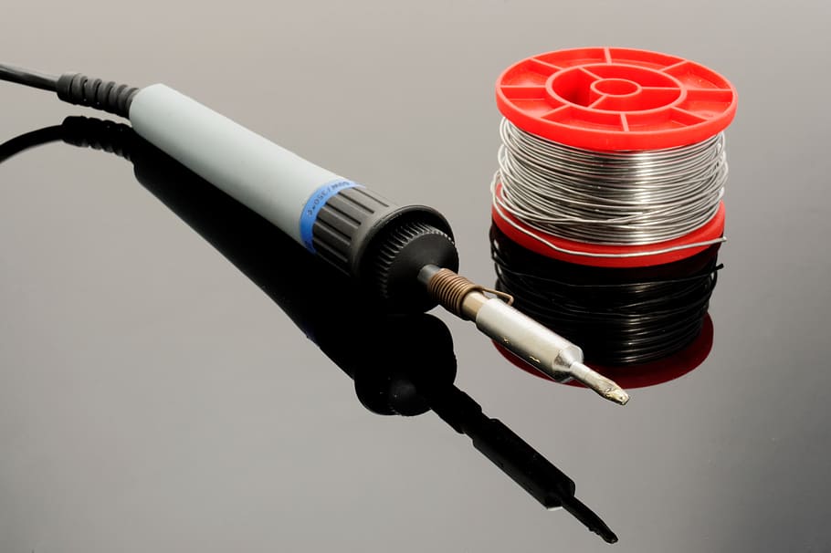 gray soldering iron and soldering lead spool on gray surface