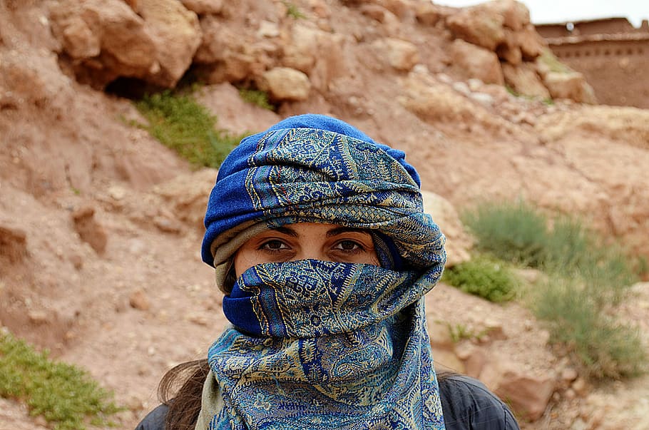 masked woman standing beside rock, woman in blue hijab headscarf