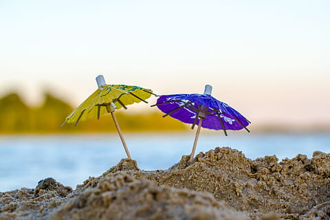 green and blue miniature umbrella stick on sand during day time HD wallpaper
