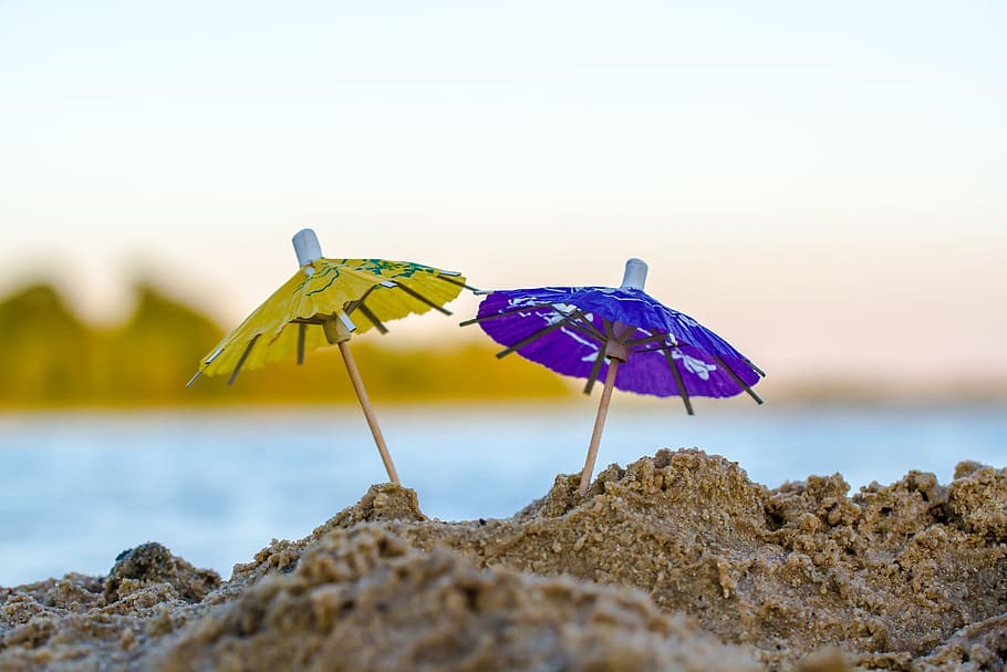 green and blue miniature umbrella stick on sand during day time HD wallpaper