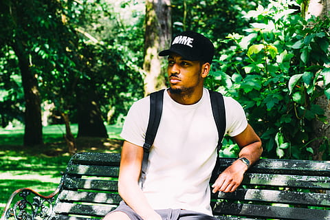man sitting on black bench while carrying black backpack in park, man sitting on bench leaning near tree HD wallpaper