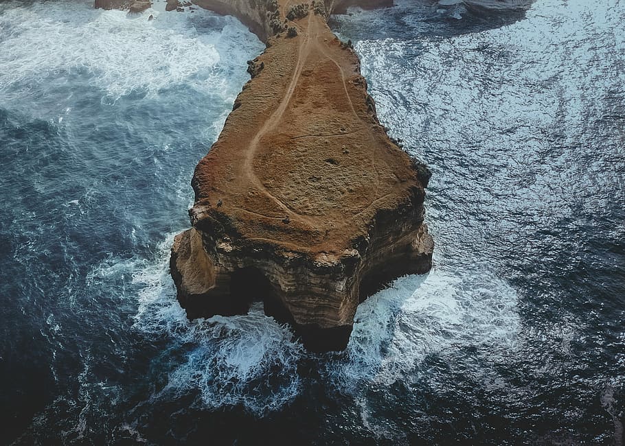 brown rocky mountain beside body of water, aerial photo of brown rock formation surrounded by body of water