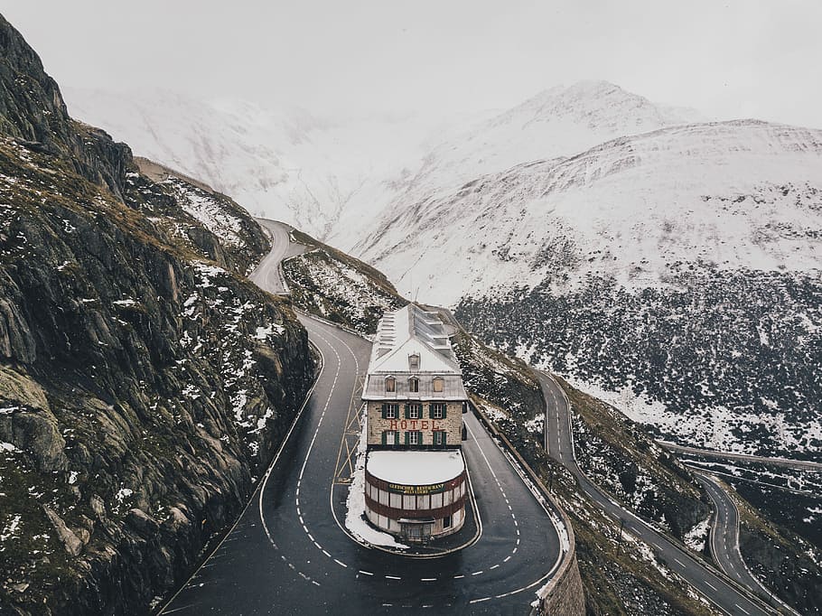 aerial view photo of concrete building near road in zig zag road, concrete building between curvy roads on mountain surrounded by snow during daytime HD wallpaper