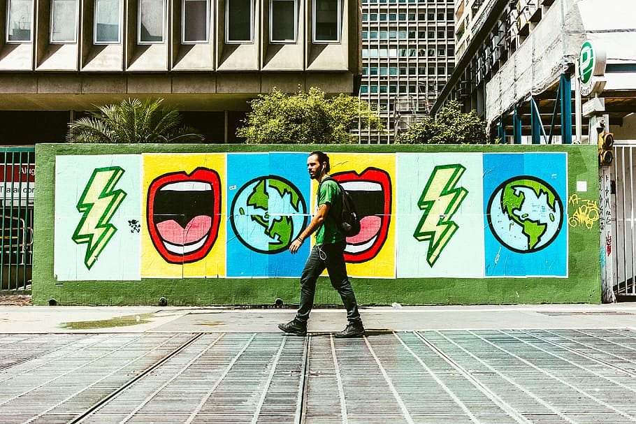 man walking on street near graffiti wall during daytime, man walking in front of graffiti HD wallpaper