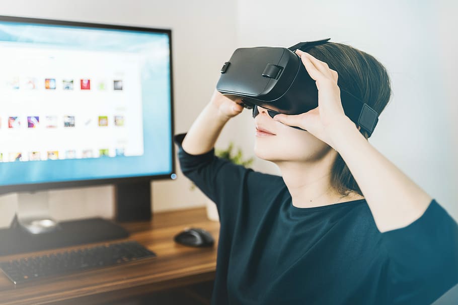 woman using black VR headset beside computer, woman using VR headset