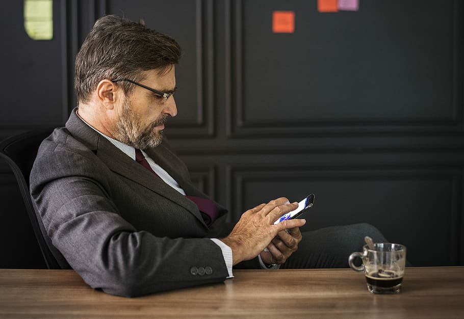 photo of man sitting on black chair using smartphone, texting HD wallpaper