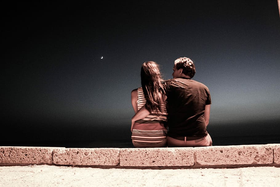 man and woman sitting on gray concrete pavement during night HD wallpaper