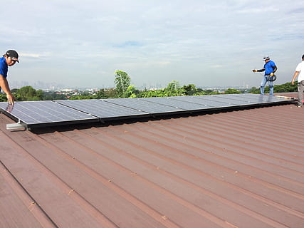 several men installing rectangular black solar panel on top of brown roof at daytime HD wallpaper