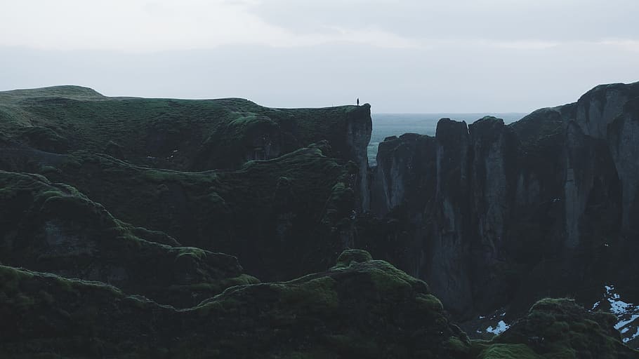 rock formations under white clouds during daytime, person standing on green and gray mountain HD wallpaper