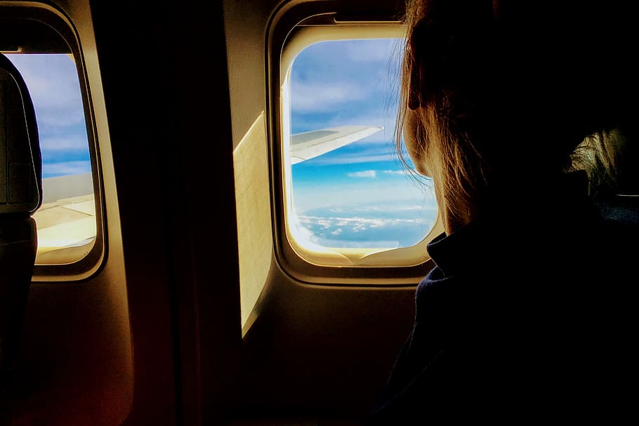 person looking outside of airplane window, person sitting inside plane while looking on window during daytime