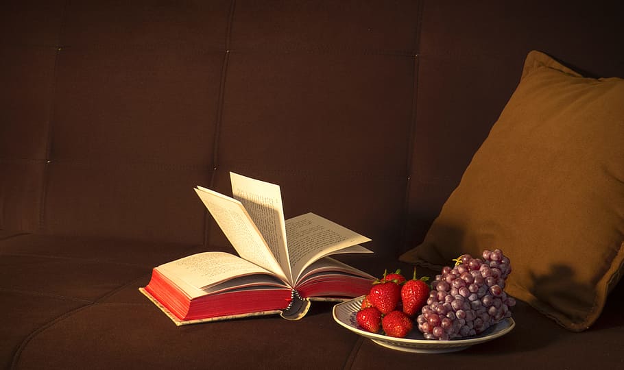 strawberries and grapes on white plate, opened book beside white plate and throw pillow HD wallpaper