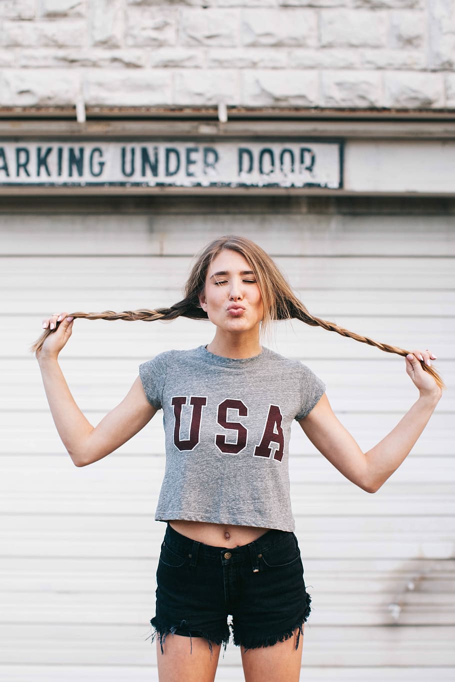 woman in gray crew-neck crop top and black denim short shorts standing behind white door during daytime HD wallpaper