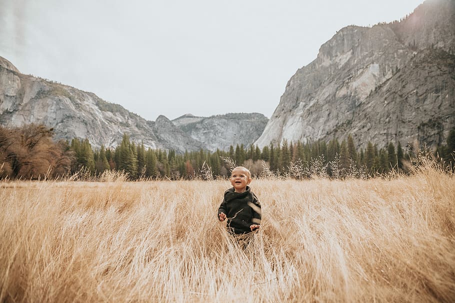 boy in black jacket stand on brown grass near mountain, photography of boy surrounding grass during daytime HD wallpaper