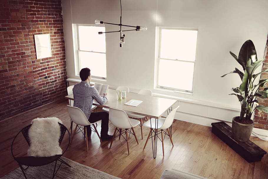 man in long-sleeved shirt reading book while sitting beside dining table HD wallpaper