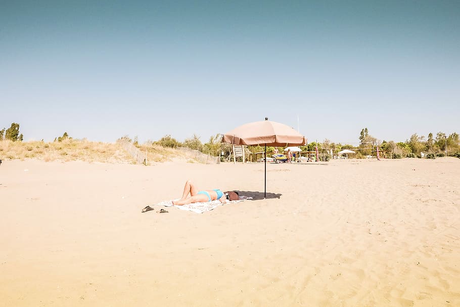 woman sun bathing under day time, person lying on sand near pink patio umbrella during daytime HD wallpaper