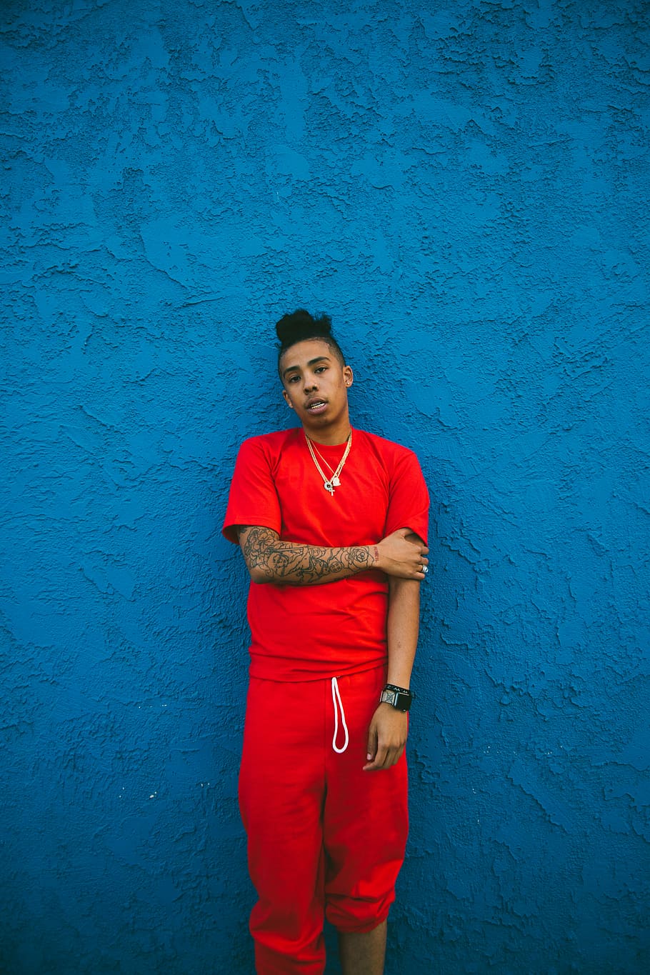 man wearing red crew-neck t-shirt and drawstring pants leaning on blue wall, man in red t-shirt and red sweatpants standing beside wall