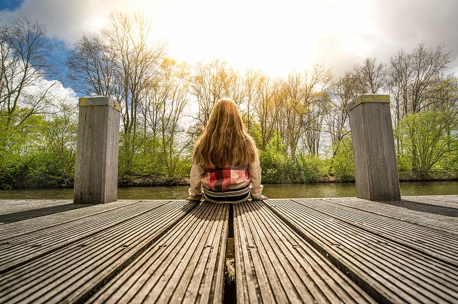 woman sitting down on brown wooden dock facing lake waters HD wallpaper