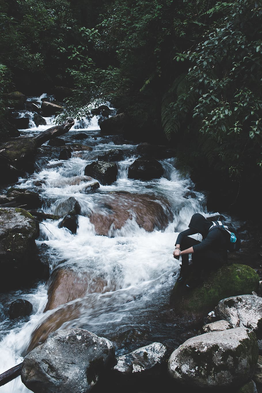 person wearing black hoodie sitting beside waterfalls, person sitting on rock beside body of water and trees during daytime HD wallpaper