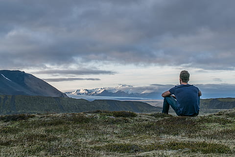 man sitting in the top of the mountain, man sitting on green field while overlooking at mountains HD wallpaper