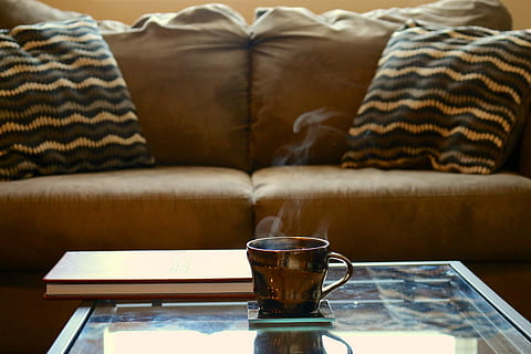 brown ceramic teacup on glass-top coffee table beside brown sofa HD wallpaper