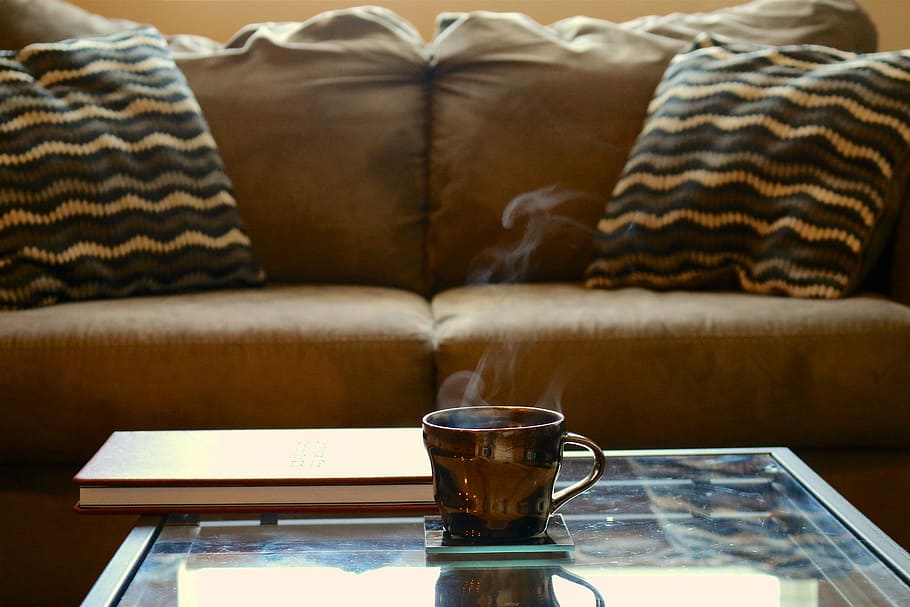 brown ceramic teacup on glass-top coffee table beside brown sofa HD wallpaper