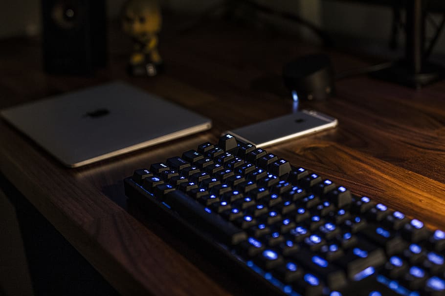 black computer keyboard on brown desk, turned on mechanical keyboard beside MacBook and iPhone on table, HD wallpaper