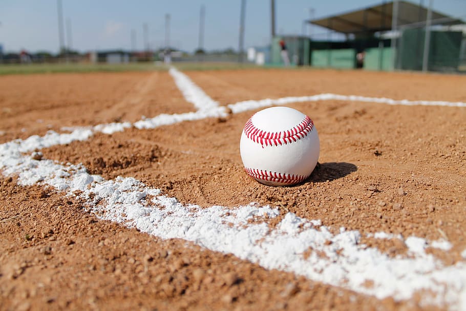 white and red baseball on brown sand, baseball field, gravel