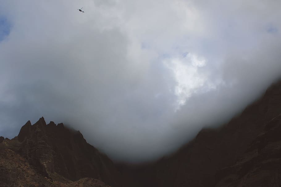 A helicopter flies through billowing clouds over a mountain landscape, mountain range under cloudy sky HD wallpaper