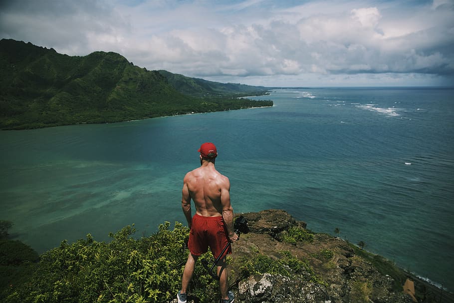 man standing on cliff surrounded by water during daytime, red