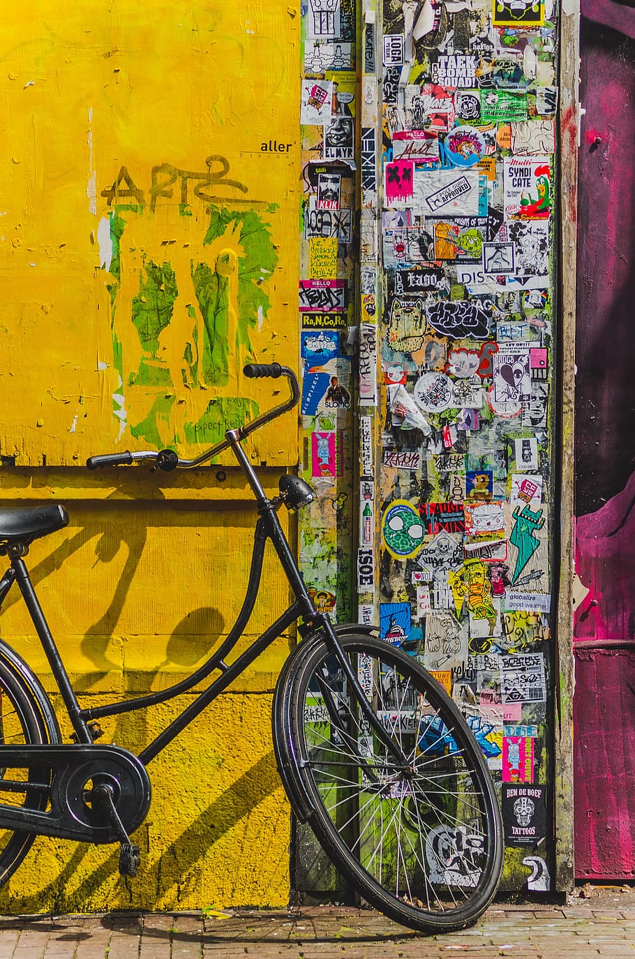 bike parked beside wall full of stickers, black city bicycle on yellow wall