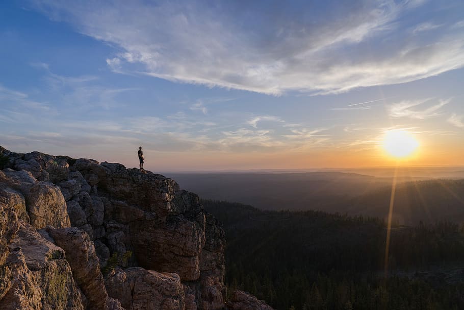 person standing on mountain cliff, person standing on brown mountain during sunset HD wallpaper
