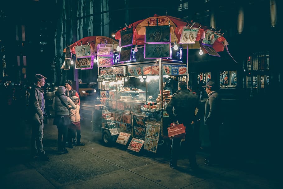 group of people standing near food cart, people gathered near the food cart at night