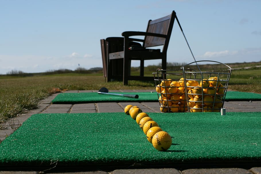 yellow golf balls near black wooden bench, driving range, line up