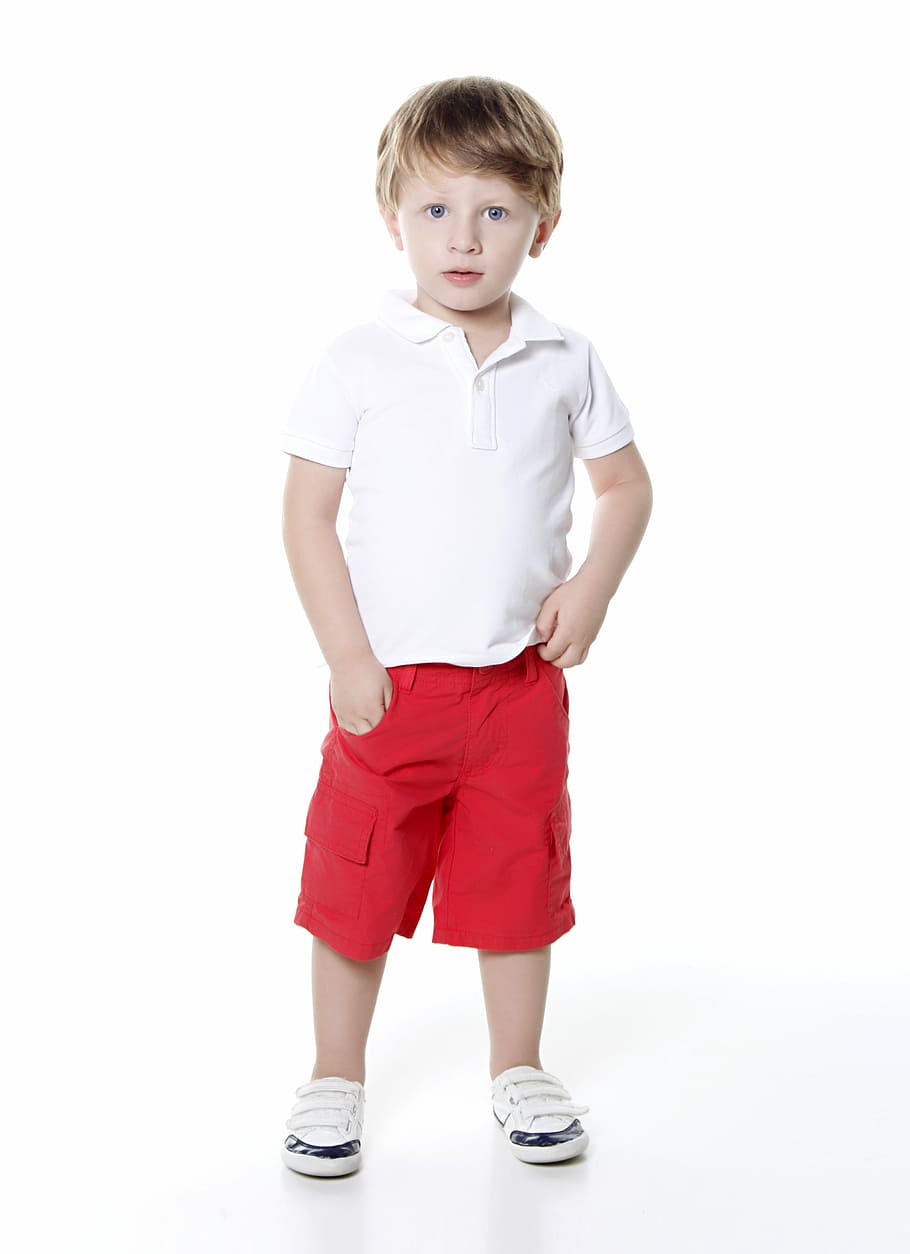 boy wearing white polo shirt and red cargo shorts standing on white surface