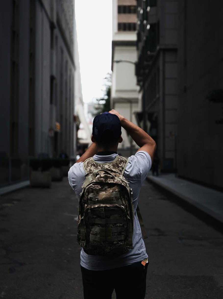 man wearing cap and backpack standing between buildings, men HD wallpaper