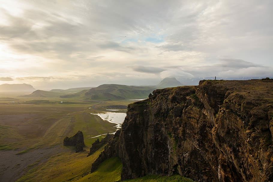rocky cliff facing green grass fields, gray mountain during daytime HD wallpaper