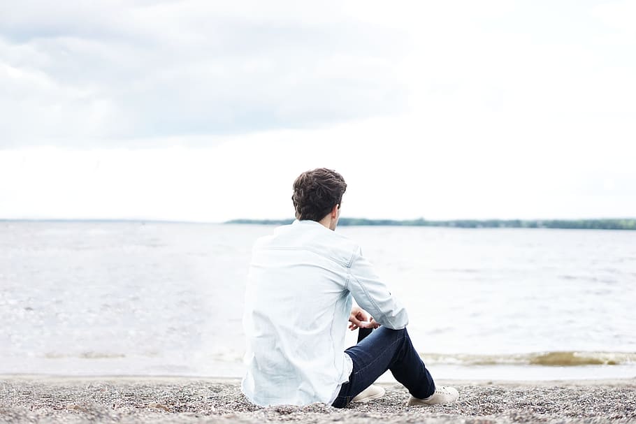 man wearing white dress shirt near sea, man sitting on sand front of sea at daytime HD wallpaper