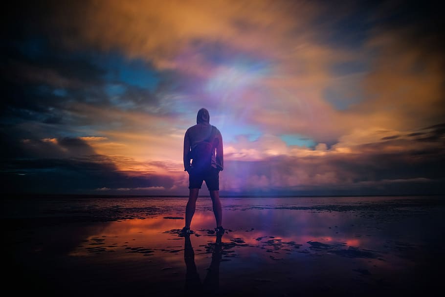 A man standing triumphant on a beach in New Romney while looking out into the water, shallow depth of field photography of man standing in the middle of field