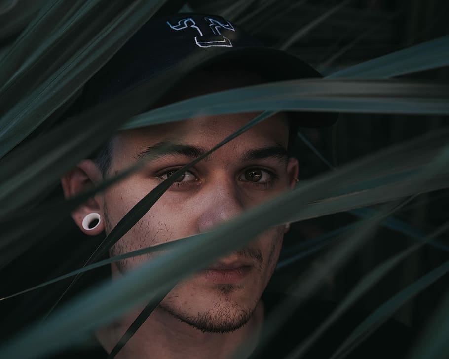 selective focus portrait photography of man wearing gauge earrings hiding at green leaves HD wallpaper
