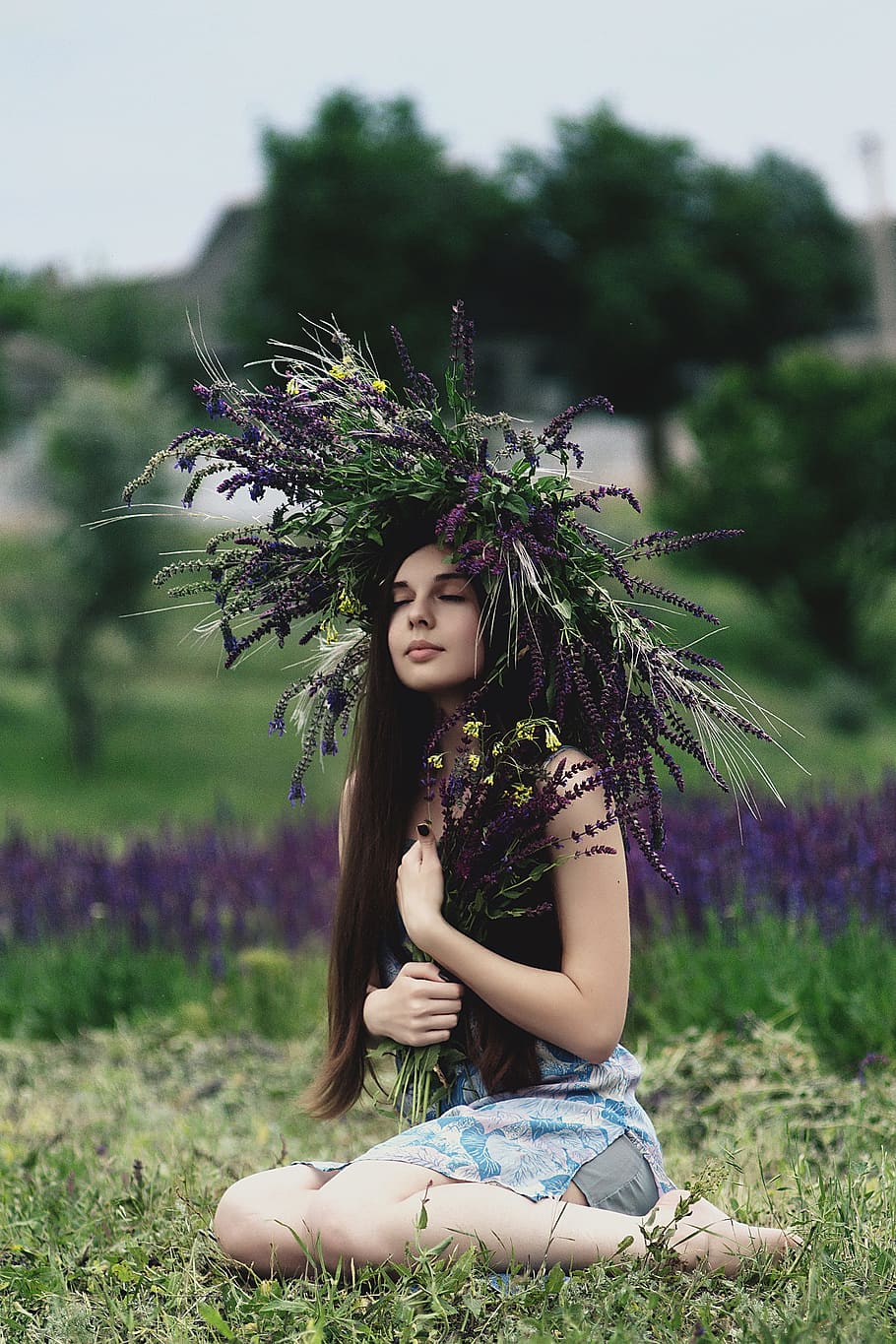 woman wearing lavender headdress sitting on grass, woman wearing black tank top near purple petaled flower