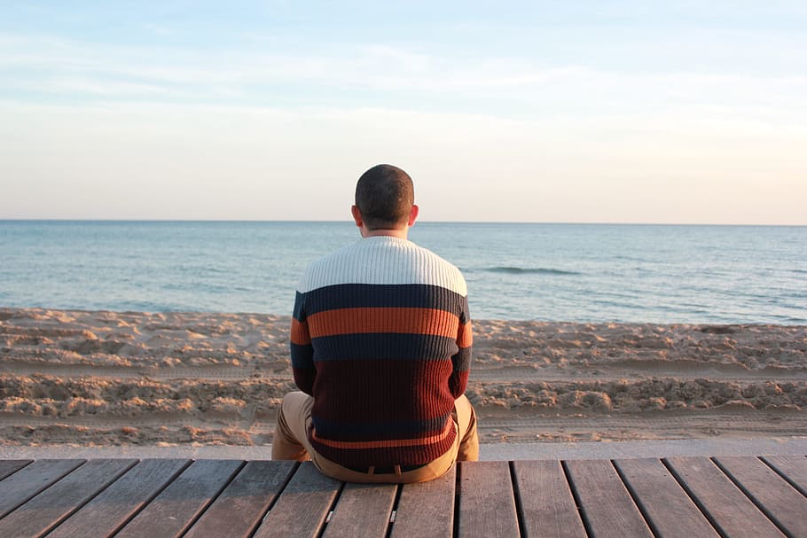 man wearing white, black, and red striped sweater sitting on brown dock HD wallpaper