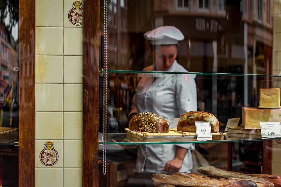 baker inside glass covered store, woman in white uniform standing inside bakeshop